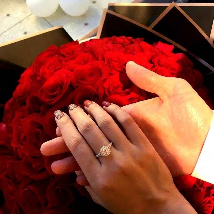 A client's halo engagement ring on her hand over a bouquet of red roses