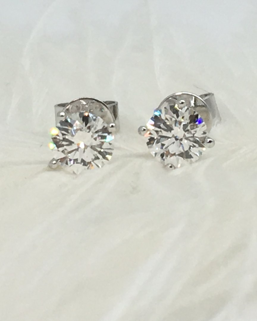 A pair of round diamond stud earrings on white feathers