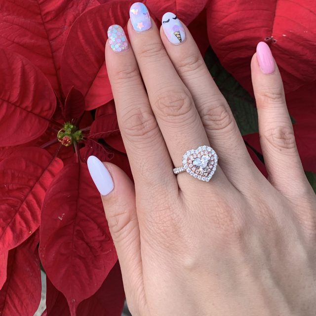 Heart-shaped double halo ring worn on a hand against red poinsettias