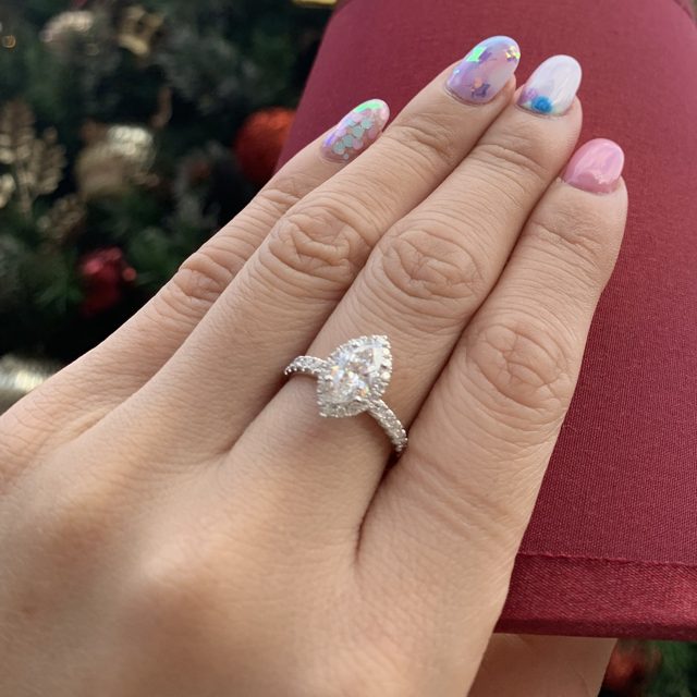 Pear-shaped halo ring worn on a hand in front of a Christmas tree