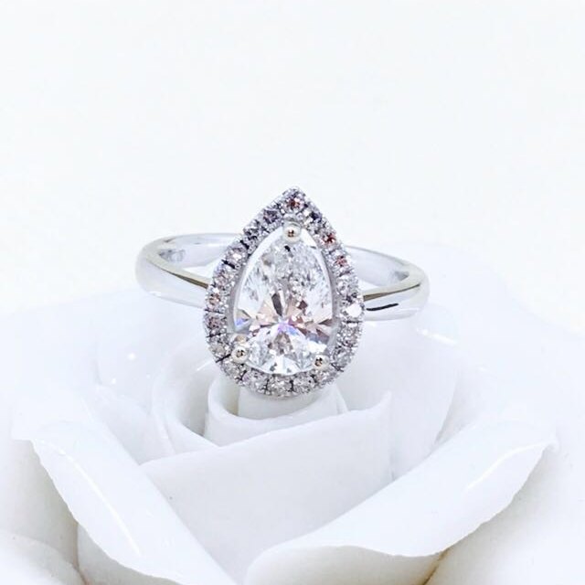 Pear-shaped diamond halo ring resting on a white rose