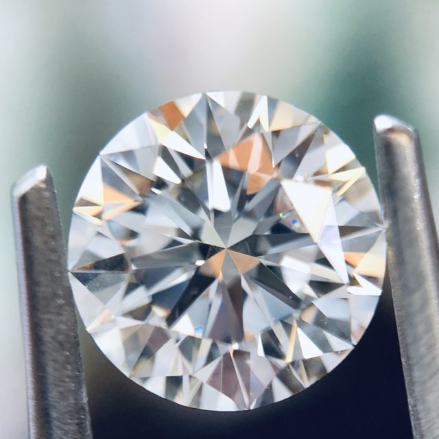 Round brilliant loose diamond held in tweezers, close up