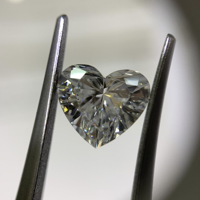 Heart-shaped loose diamond held in tweezers, viewed under a loupe light
