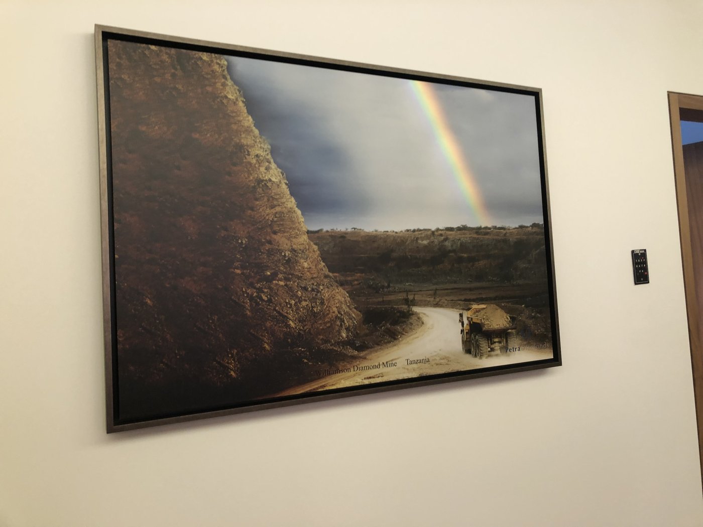 A framed photograph of an open-pit diamond mine with a rainbow, hanging in a mining company's office