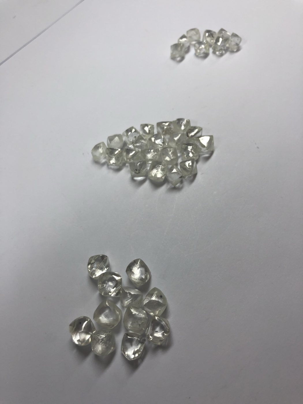 Three piles of rough diamonds sorted by size on a white table